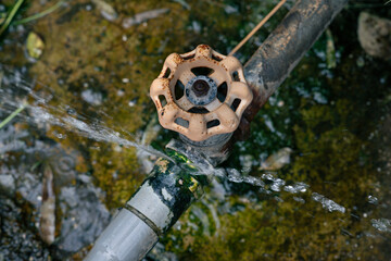 Rusty water tap attached to a pipe with water flowing out and leaking at the connection
