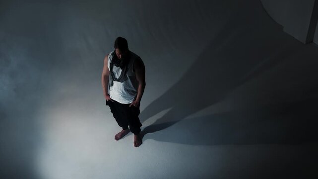 A pensive male figure stands alone against a stark white void. Harsh lighting projects two clear shadows behind him, metaphorically representing the complex layers of human identity and internal confl