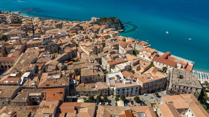 Naklejka premium Aerial panorama of Tropea’s historic center, showcasing a dense tapestry of terracotta roofs and stone buildings perched above the vibrant turquoise sea and the iconic Santa Maria dell’Isola sanctuary