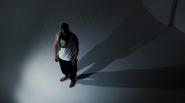 Under intense, contrasting light on a featureless white backdrop, a contemplative young man casts two stark shadows, visually exploring the theme of psychological duality and self-knowledge.
