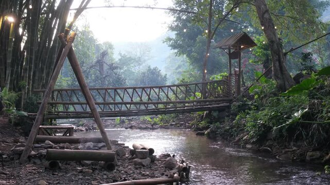 A woman walking across a wooden bridge with a canal flowing in the forest