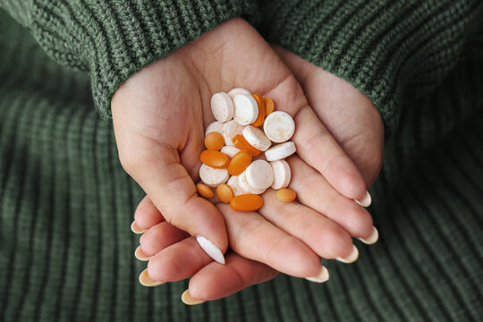 Hands holding mixed white and orange pills closeup. Variety of prescription tablets in female palms. Medication overdose risk and polypharmacy concept. Drug interaction and self medication.