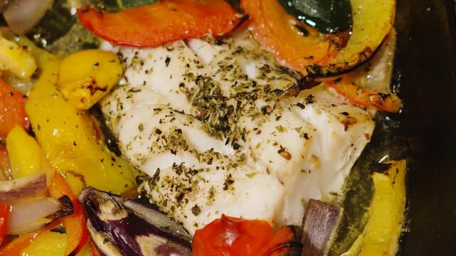 Freshly cooked traybake of wild caught atlantic Cod fillets with mediterranean diet vegetables. Peppers, onions, courgette, tomatoes with herbs. High quality healthy food videography.