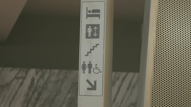 Close up of modern indoor wayfinding panel showing bed elevator stairs restroom symbols wheelchair access and direction arrow in minimalist interior