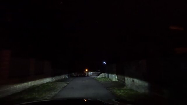 Night drive through narrow residential street illuminated by car headlights