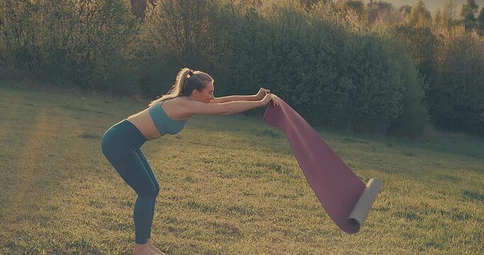 Woman Unrolling Yoga Mat in Park on Sunny Spring Day