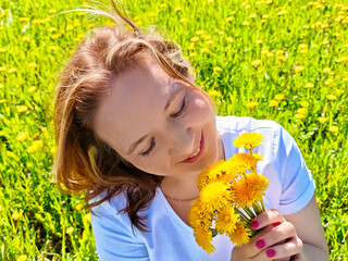Woman enjoying a sunny day in a field of dandelions while holding vibrant yellow flowers in her hands