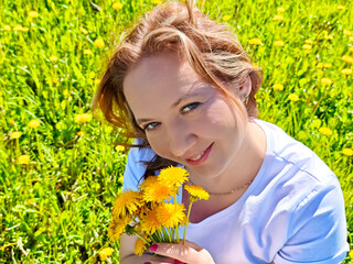 Woman smiles brightly while holding yellow flowers in a vibrant green field on a sunny day