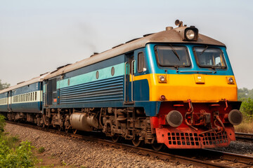 Obraz premium Vibrant Indian railway locomotive racing across green countryside, yellow stripe and turquoise accents symbolizing travel, energy and freedom