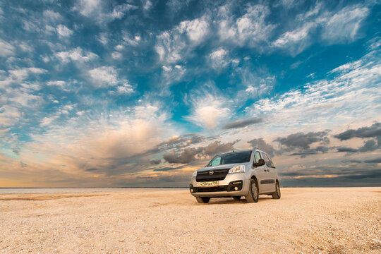 Silver opel combo car parked on sandy beach under dramatic cloudy sky. Taganrog. Russia. May 20, 2024