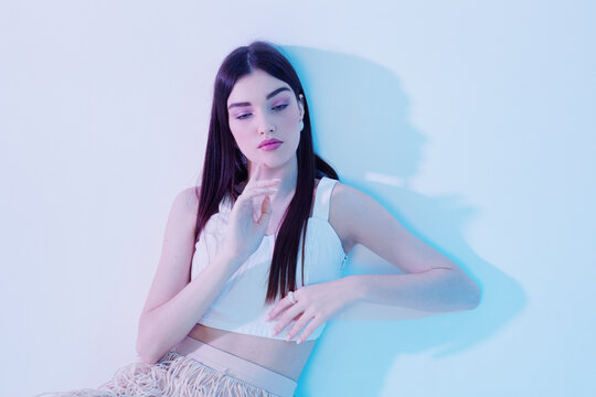 Young woman with long dark hair poses in a white top against a light background. Soft lighting highlights her beauty and fashion style. Concept for beauty and fashion.