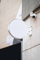 Blank circular outdoor sign mockup mounted on a wall with security camera, creating a template for brand identity, advertising, and corporate signage display