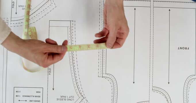 Professional woman seamstress methodically measures pattern details with measuring tape. Meticulous female tailor checks width and height of pattern pieces