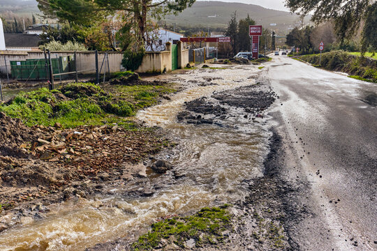 View of muddy water flowing across the road near structures, creating a scene of earthy tones against the stark asphalt, Setenil de las Bodegas, Andalusia, Spain.
