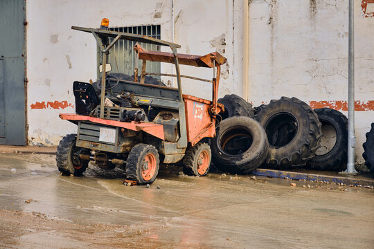 View of a vintage dumper truck, standing still on the wet pavement, framed by stacked tires and a weathered building facade, Setenil de las Bodegas, Andalusia, Spain.