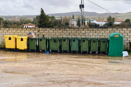 View of a row of colorful recycling bins lining a brick wall under a cloudy sky, Setenil de las Bodegas, Andalusia, Spain.