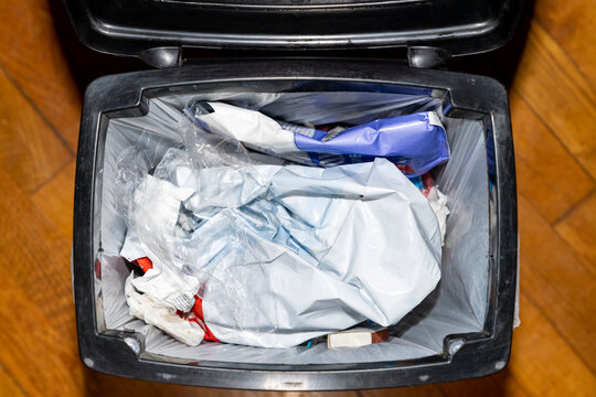 Trash bin filled with plastic packaging and household waste inside a kitchen. Overhead view photography. Household waste management and recycling concept.