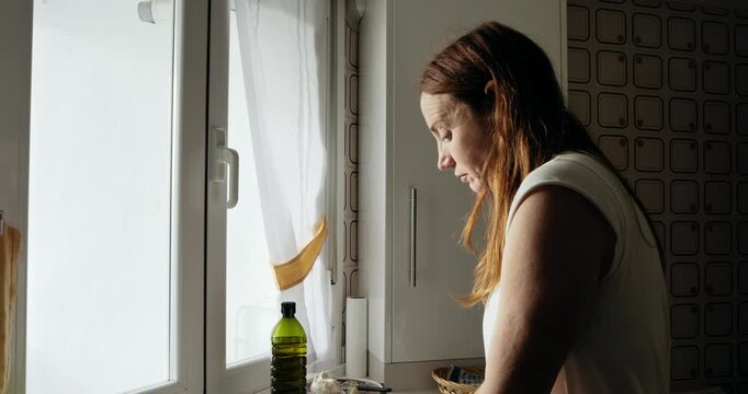 On a cold winter morning, a mature woman looks pensively out of the kitchen window as she eats toast and drinks coffee with milk.