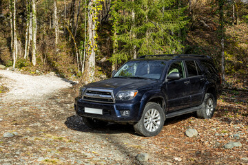 Black off-road SUV parked on a rough dirt and gravel road in a rugged mountain forest wilderness. © NastyaPhoto