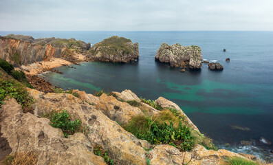 Fototapeta premium View of the sea with rock formations next to Somocuevas Beach, in the Costa Quebrada Geopark, Cantabria, Spain, on a cloudy summer day.