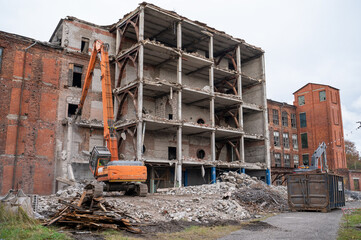 Fototapeta premium Excavator with demolition attachment breaks apart building while standing on pile of rubble