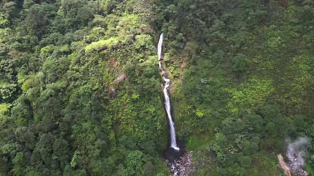 Top down aerial perspective of Curug Cikawah waterfall cascading through steep green cliffs and tropical vegetation in Bogor, Indonesia. Dramatic natural scenery ideal for travel and nature themes.