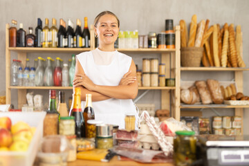 Fototapeta premium Female employee near store counter and waits for visitors. Seller wants to sell large amount of alcohol, increase average check. Large amount of food, pile of delicious are on counter
