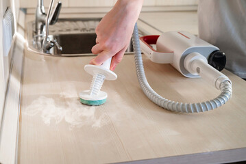 Cleaning a kitchen sink with a handheld steam cleaner during a home cleaning session