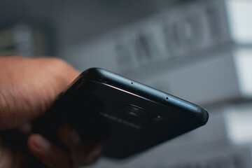 Hand Holding Black Smartphone Top View Detail in Minimalist Setting. High-angle close-up shot of a...