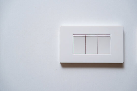 Modern white triple light switch on a clean white wall with copy space. Minimalist interior design and electricity concept.
