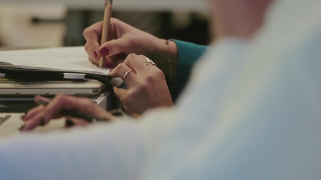 Person writing notes in journal on table beside stacked books