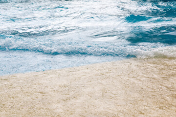 Obraz premium Gentle ocean waves lapping against a sandy beach under a bright sky, showcasing the natural beauty of coastal scenery