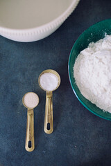 Close-up of measuring spoons with salt and dry yeast beside a flour bowl on dark background. Ideal for culinary, food photography, and baking projects.
