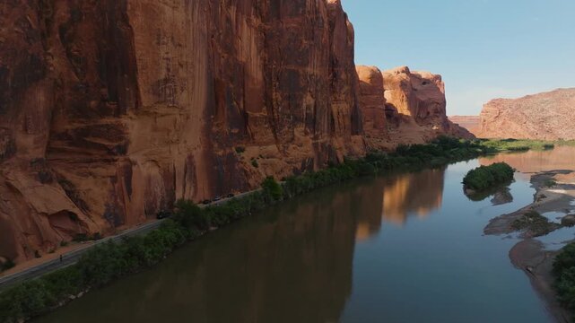 Aerial view of the serene river flowing between the towering red rock cliffs, reflecting the clear sky, Moab, Utah, United States.