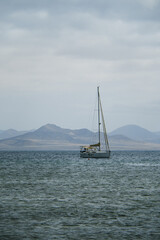 Fototapeta premium A solitary sailboat anchored on calm rainy coastal waters with hazy mountains in the background, evoking tranquility and open space.