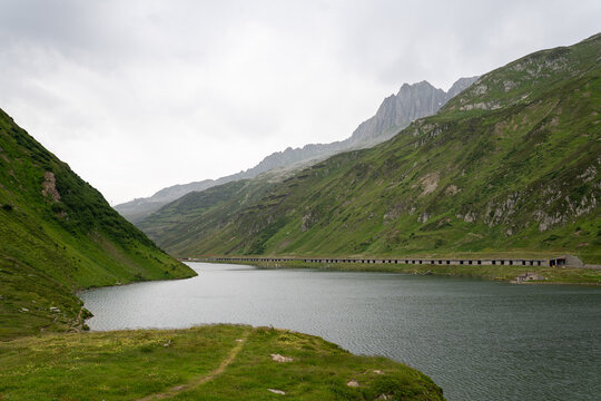 Serene mountain lake surrounded by lush green slopes and rugged peaks under an overcast sky, showcasing a calm alpine landscape and wide open scenery.