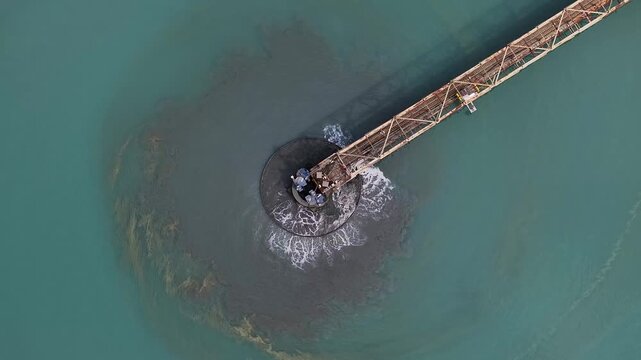 Aerial view of a rusty pier extending into turquoise waters, contrasting with the dark sediment stirred around its base, Arizona, United States.