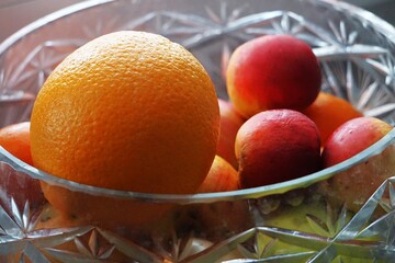 Pomarańcza i jabłka ułożone w kryształowej misie, zbliżenie na naturalne kolory, przejrzyste szkło i świeżą strukturę owoców w miękkim świetle.  © Adam