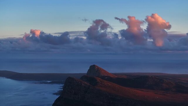 Aerial view of three majestic peaks meet the ocean under a sky brushed with soft pink clouds, where land and sea merge in a symphony of color, Cape Town, South Africa.