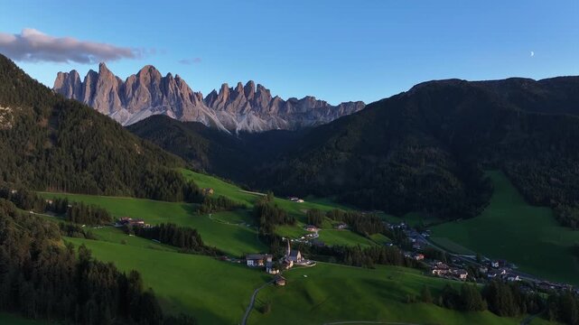 Aerial view of Santa Magdalena village nestled amidst rolling green hills and towering mountains, a scenic landscape, Santa Magdalena, Trentino-Alto Adige, Italy.