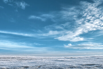 Winter frost on field under blue sky with wispy clouds
