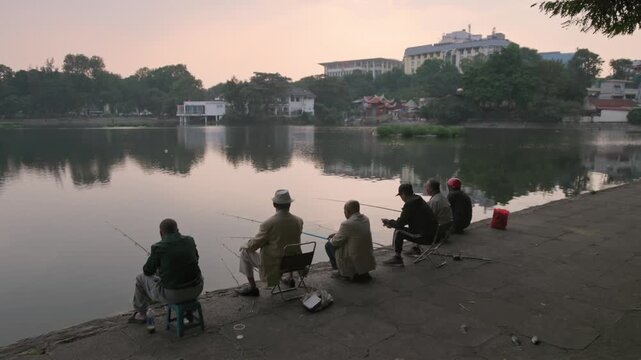 In Hanoi, Vietnam, a group of men fish together at Thien Quang Lake. They are enjoying a relaxing morning activity, connecting with nature and each other in their community.