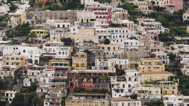 Aerial view of buildings with white and colourful walls, and dark windows cascading down a steep hillside, creating a vibrant urban tapestry, Positano, Campania, Italy.