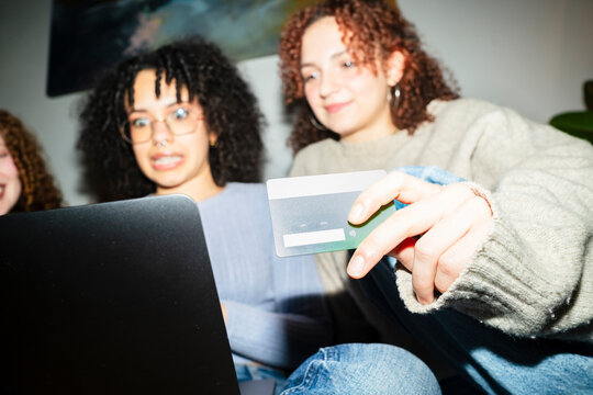 Three young women are looking at a laptop screen and holding a credit card, suggesting online shopping or a financial transaction.