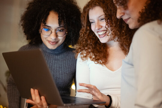 Three young women of diverse backgrounds gather around a laptop, sharing a moment of laughter and collaboration.