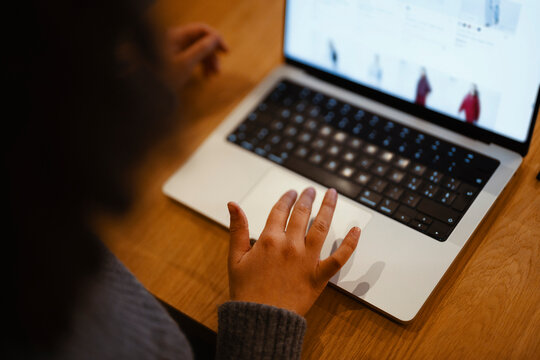 A person's hand rests on a laptop's trackpad while browsing an online store. The screen displays clothing items for sale.