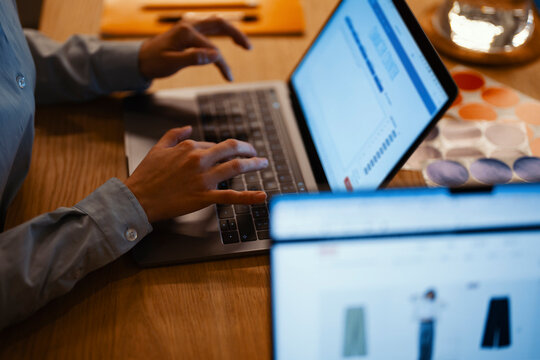 A person's hands are typing on a laptop, with another screen showing clothing items. This depicts online work or shopping.