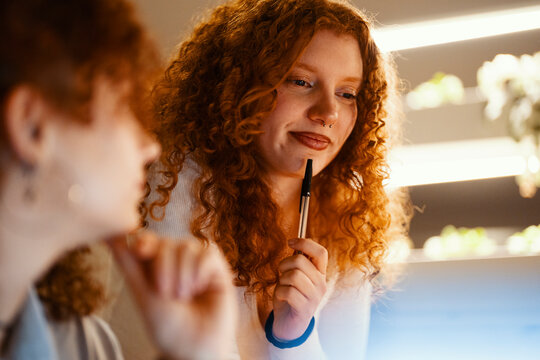Two young women with curly red hair collaborate on a project, one holding a pen thoughtfully as they discuss ideas.