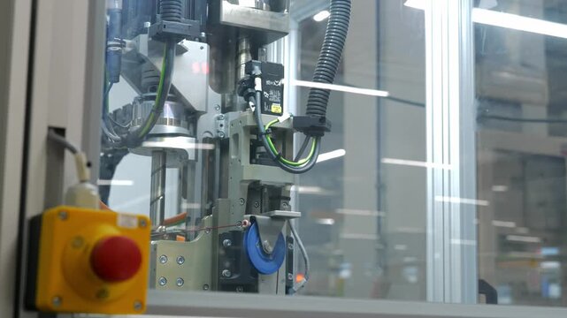 Precision robotic assembly machine in operation with emergency stop button and mechanical parts in a modern high tech industrial manufacturing factory environment