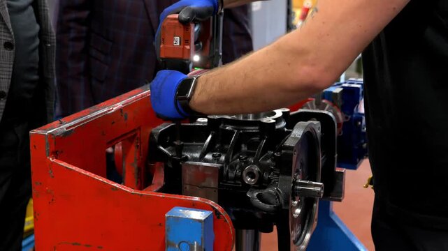 Close up of an industrial worker using a professional electric power screwdriver to assemble a heavy metal engine part in a manufacturing factory environment